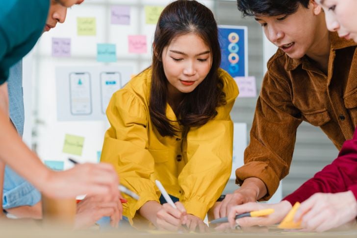 Image shows a group of people drawing together with a kanban board in the background