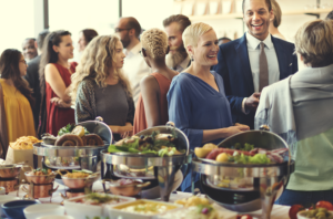 Image shows a gathering of people beside a long table laden with dishes of different types of food
