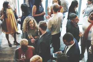 Image shows a gathering of people from above holding wine glasses