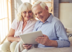 Image shows smiling older woman and man looking down at a tablet