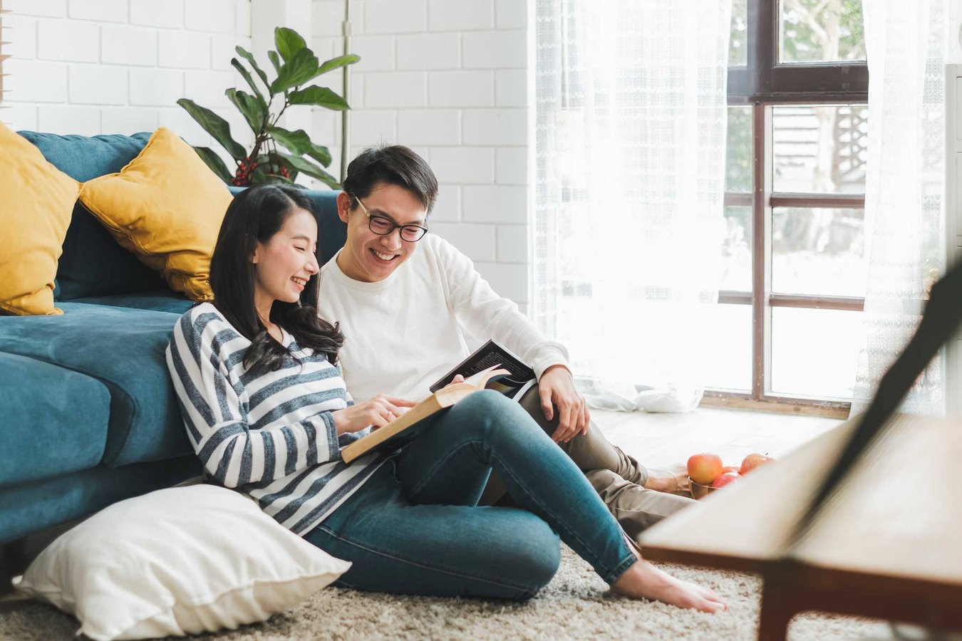 Image shows a young woman and man on the floor in front of a sofa reading and pointing at the page