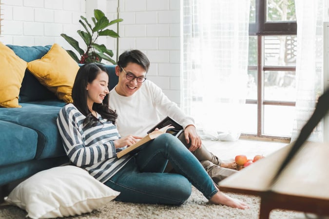 Image shows a young woman and man on the floor in front of a sofa reading and pointing at the page