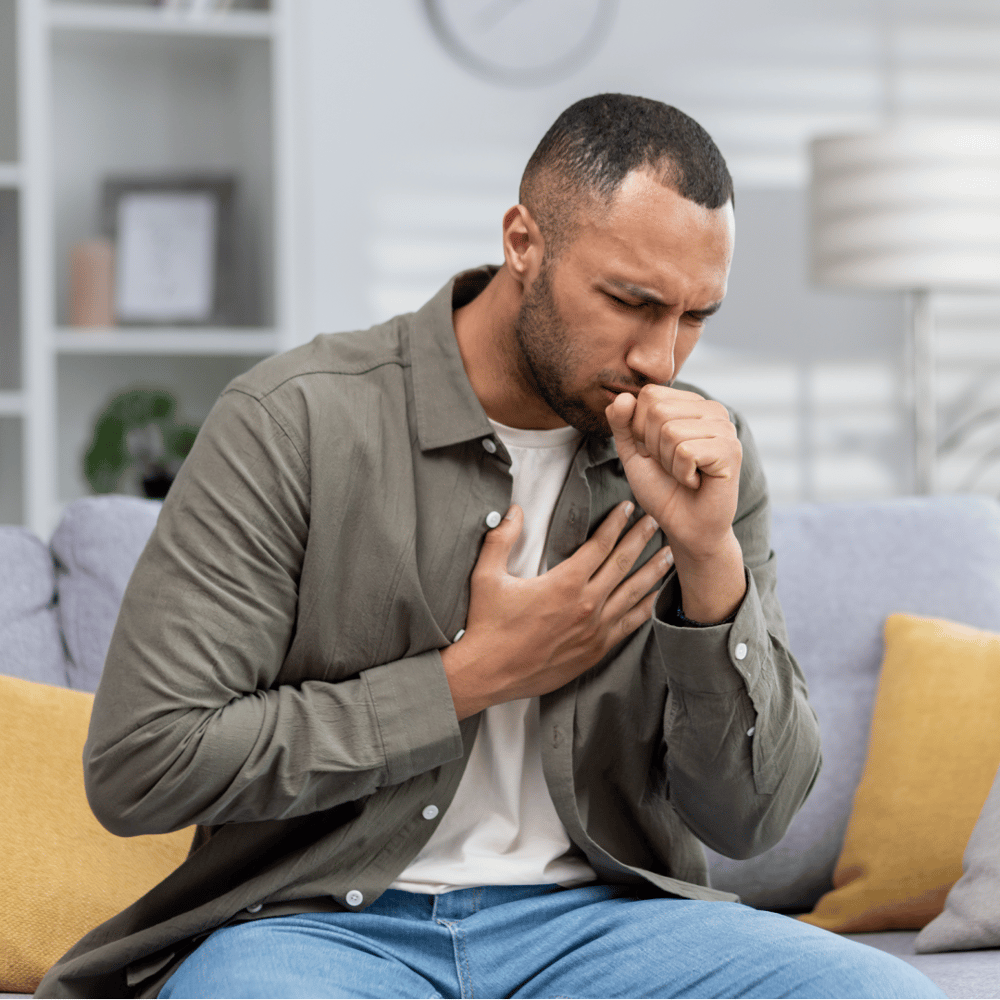 Person sitting on a sofa looking unwell and coughing, representing sickness absence and the impact of ill health on employees.