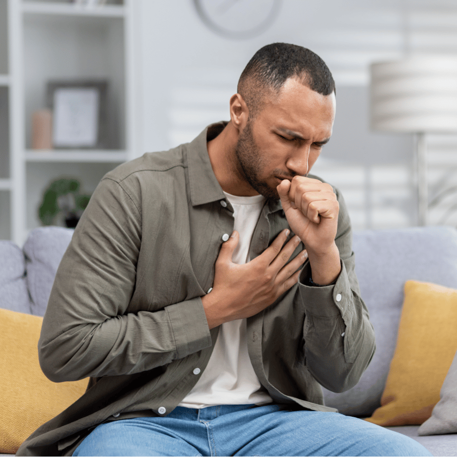 Person sitting on a sofa looking unwell and coughing, representing sickness absence and the impact of ill health on employees.