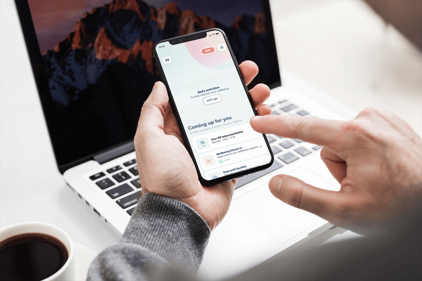 Image shows a a phone in someone's hands in front of a laptop