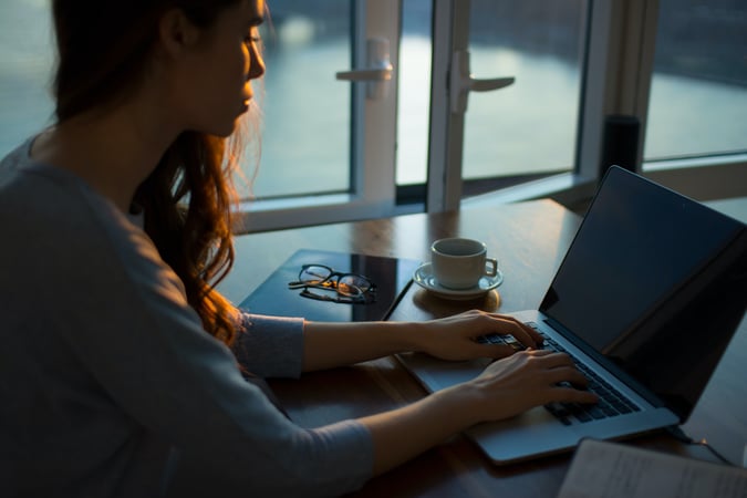 Woman typing  on laptop by a window at dusk