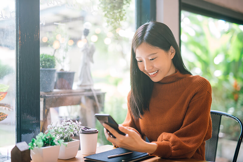 Woman sitting at a table smiling at her phone