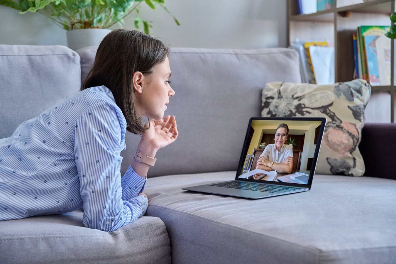 Woman on a sofa at home having a video counselling session with a smiling counsellor on her laptop.