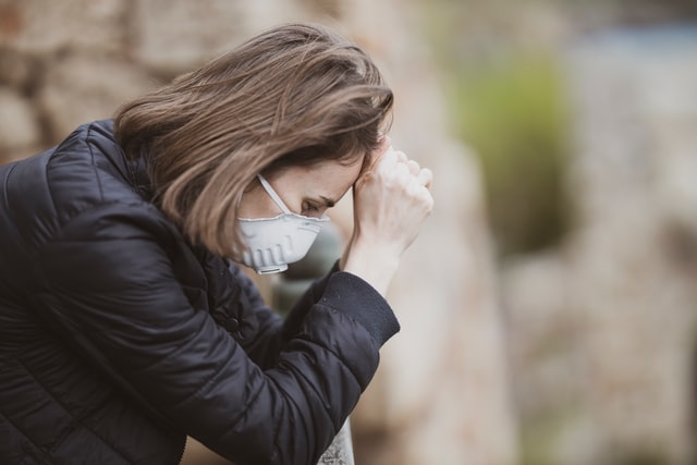 Image shows woman outdoors leaning on a railing wearing a mask