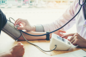 Images shows an arm in a blood pressure cuff with someone in a white coat holding the sensor of a stethoscope to the cuff